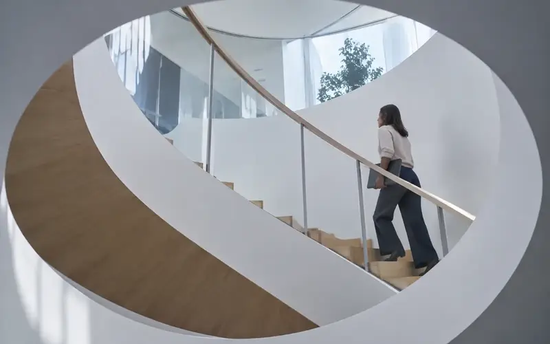 An office stair and landing with one person walking up in profile, the stairwell void above