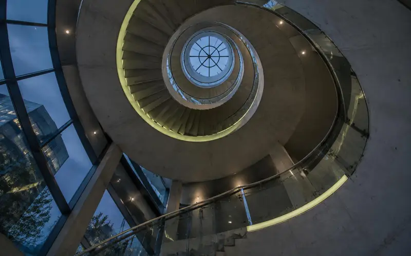 A technology office atrium at dusk with no people, seen looking up a spiral staircase